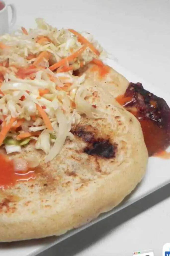 A plate of freshly cooked chicken pupusas served with a side of vibrant curtido (cabbage slaw).