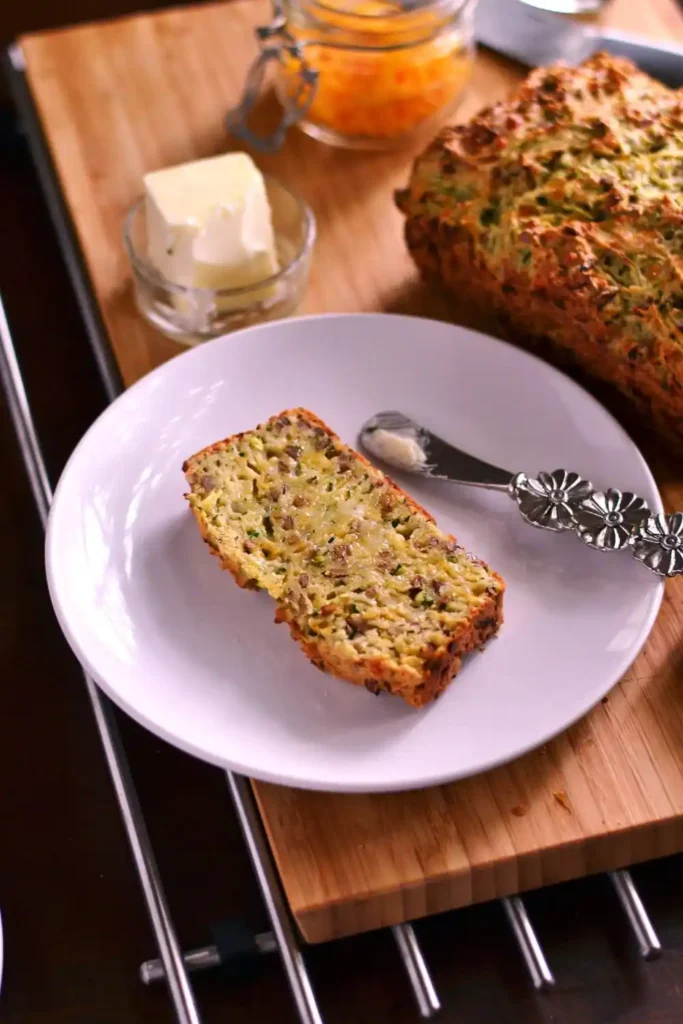 "A freshly baked loaf of zucchini bread on a wooden cutting board, with a few slices cut to show the moist, spiced interior flecked 