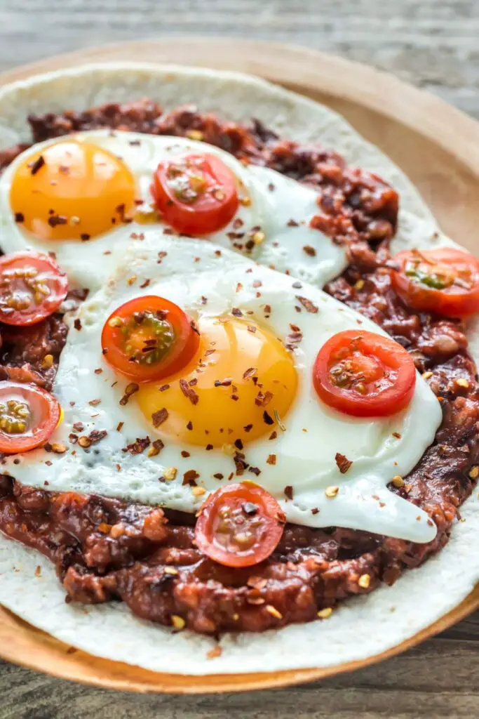 A white plate with baked huevos rancheros, featuring a baked egg in a rich tomato sauce topped with fresh cilantro