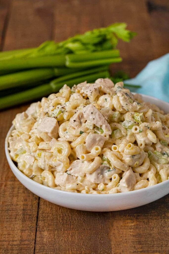 Colorful chicken pasta salad with vegetables, herbs, and a light dressing, served in a white bowl.