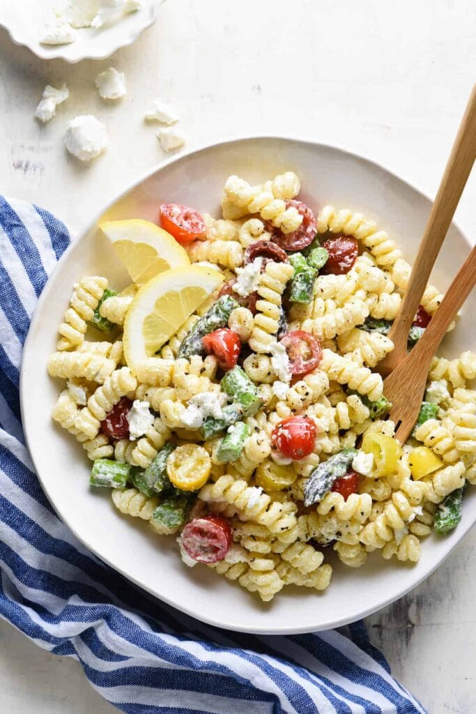 A bowl of Goat Cheese Pasta Salad featuring spiral pasta, creamy crumbled goat cheese, cherry tomatoes, fresh spinach leave