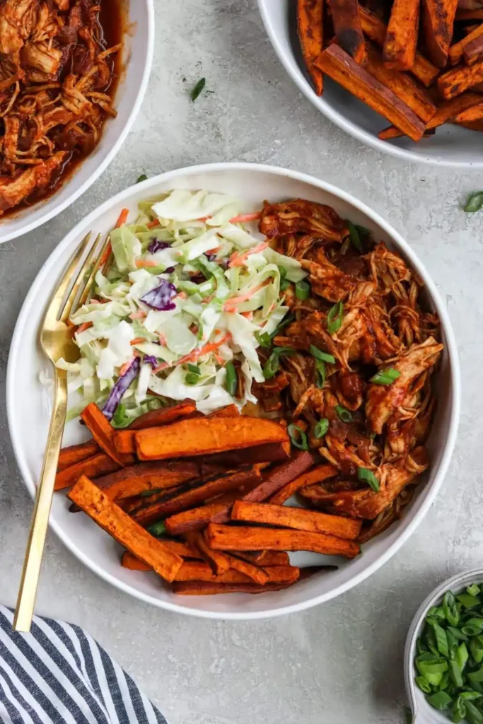  bowl featuring shredded BBQ chicken, colorful vegetables, and a side of fresh coleslaw, topped with a tangy dressing.