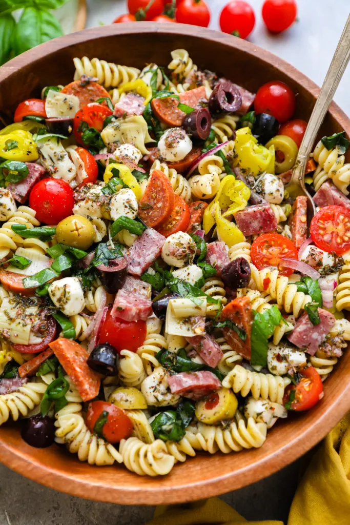 A vibrant Italian Antipasto Pasta Salad, featuring rotini pasta tossed with cherry tomatoes, black olives, artichoke hearts, diced salami, mozzarella balls, and fresh basil leaves. 