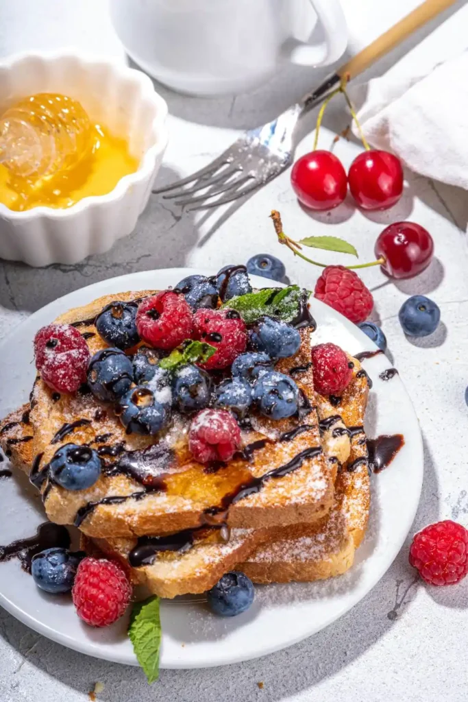 Mixed Berry French Toast Bake on a white plate, adorned with fresh strawberries, blueberries, and raspberries, 