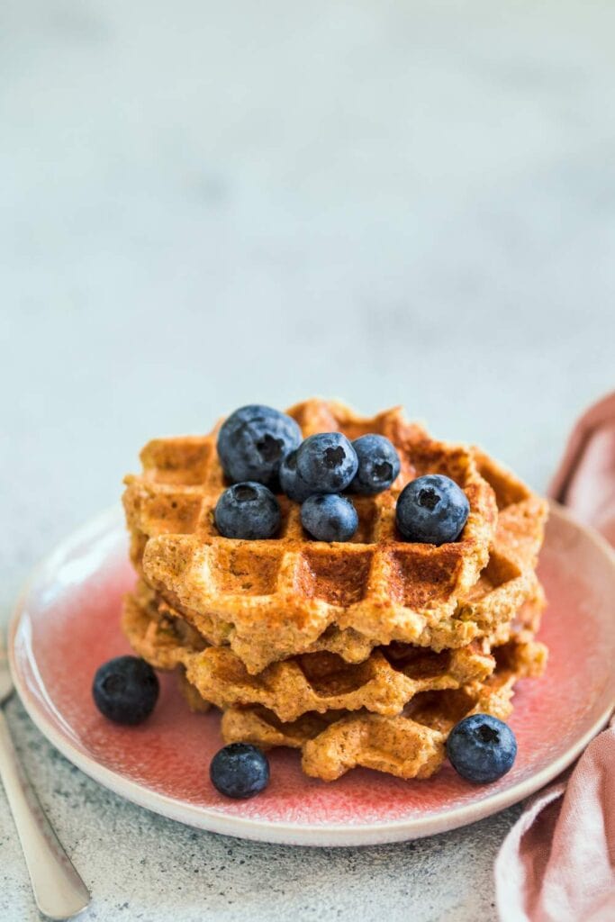 A stack of golden-brown oat waffles served on a white plate, garnished with fresh berries and a drizzle of maple syrup