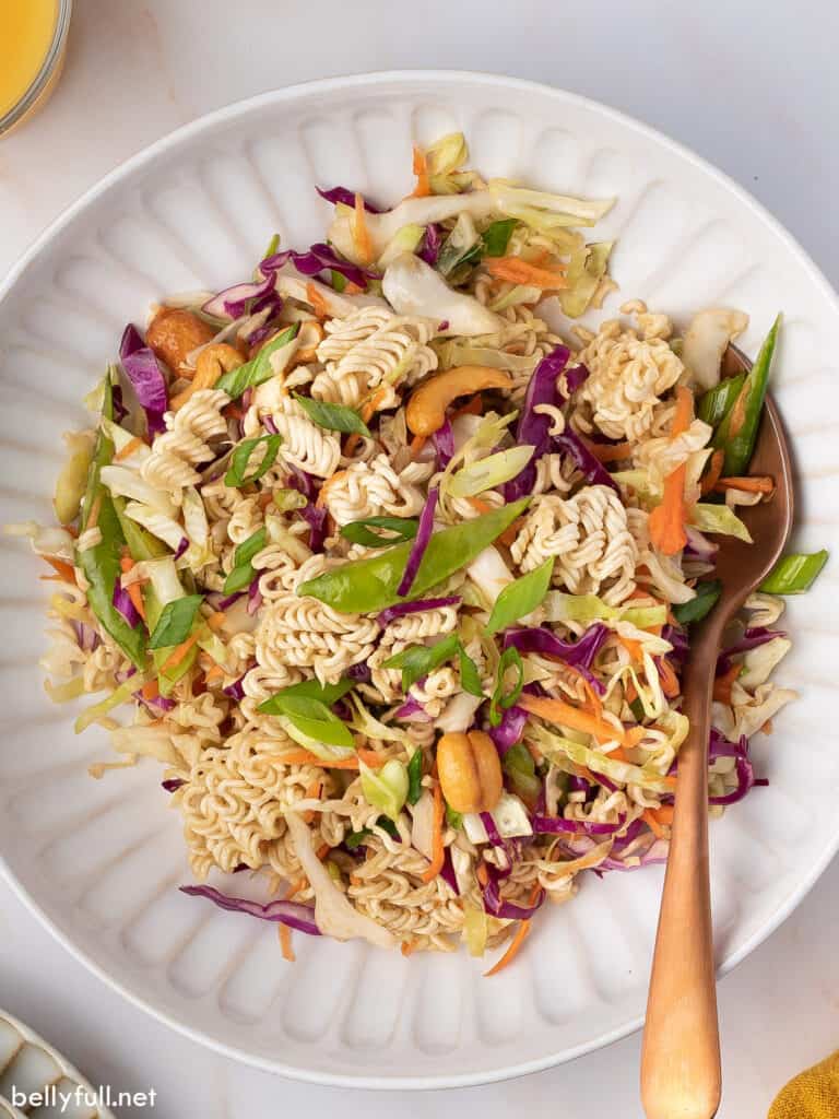 bowl of ramen noodle salad topped with colorful vegetables, sesame seeds, and a drizzle of dressing.