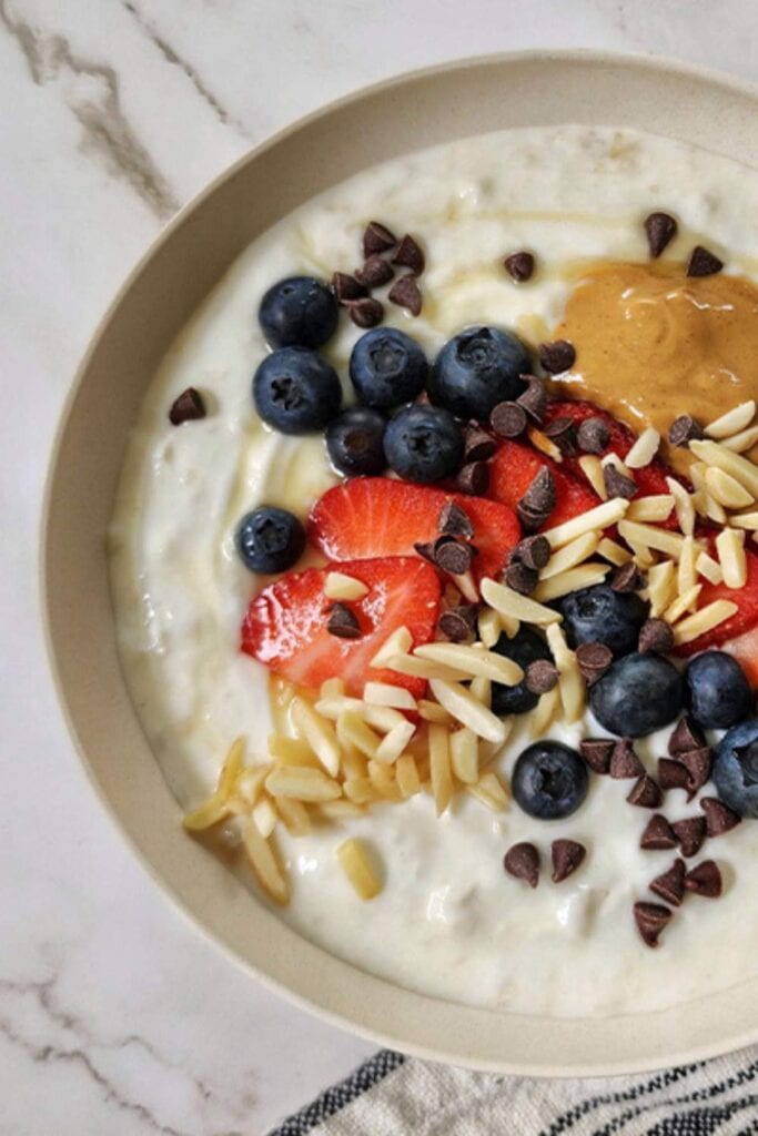 A bowl of creamy yogurt topped with fresh strawberries, a drizzle of peanut butter, and a sprinkle of granola