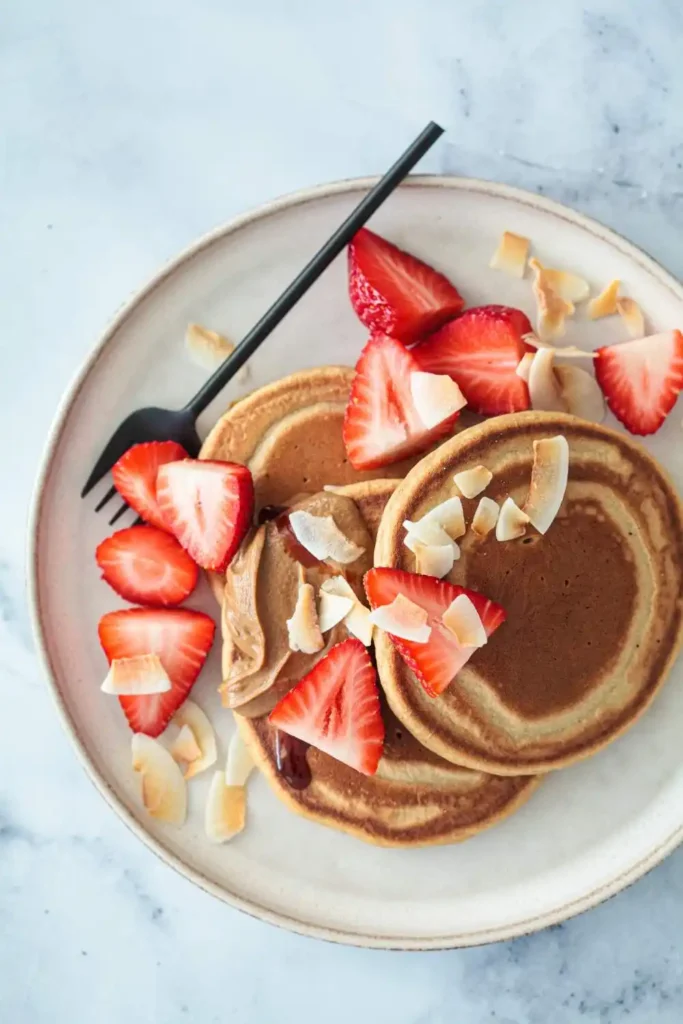 Vegan Strawberry Pancakes topped with fresh strawberries and a drizzle of maple syrup, served on a white plate with a fork.