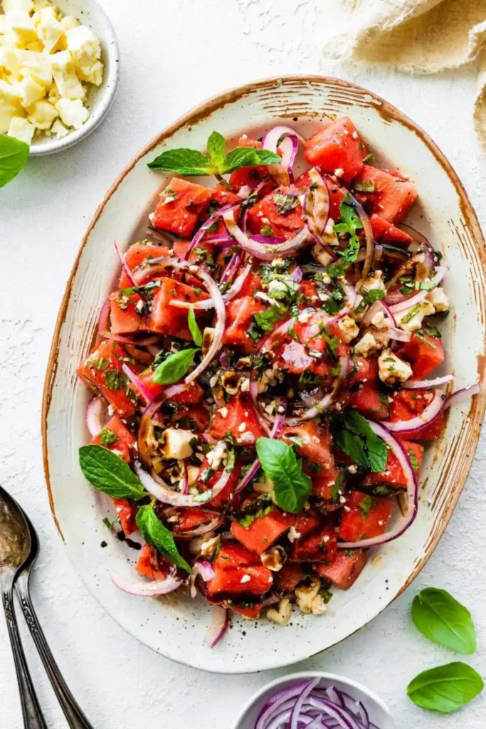 Refreshing watermelon salad topped with crumbled feta cheese and fresh basil leaves, served in a white dish