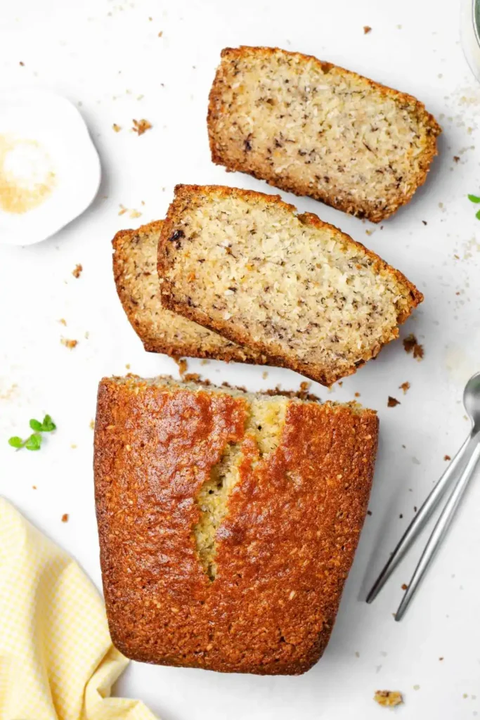 A freshly baked loaf of banana bread with a golden-brown crust and a few sliced bananas on top, resting on a cooling rack