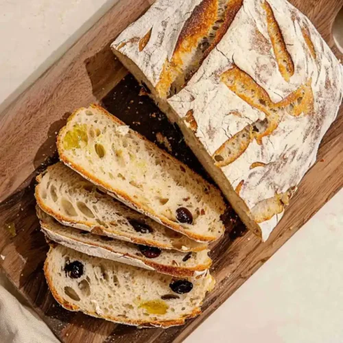 Mediterranean Olive Oil Bread and two slices are cut from loaf and is place on wooden board