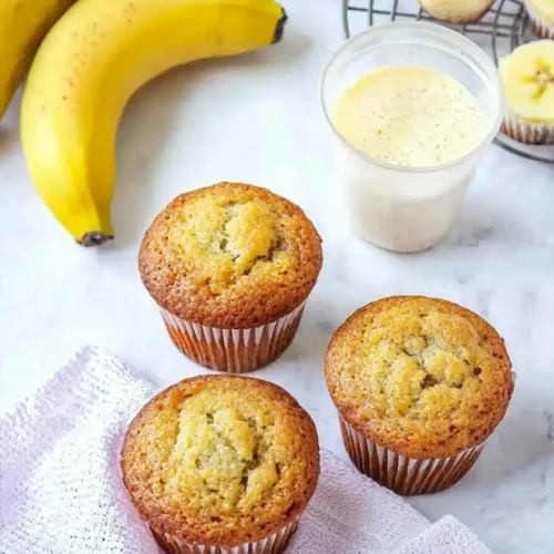 three Banana Muffins is placed on white napkin and three bananas are placed nearby