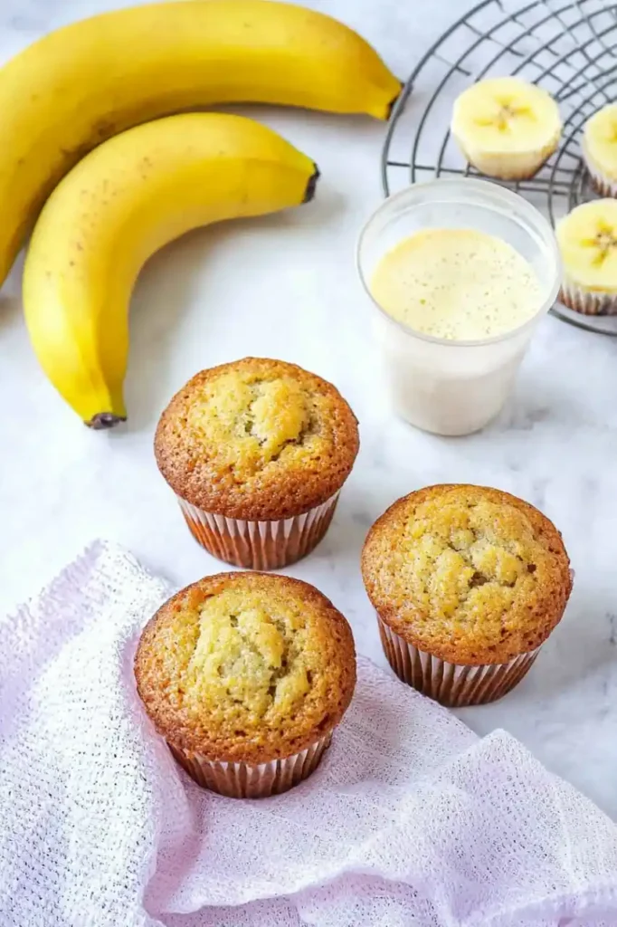 three Banana Muffins is placed on white napkin and three bananas are placed nearby