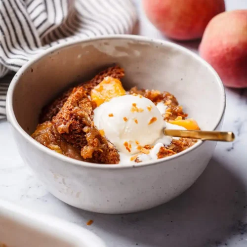 warm serving of peach cobbler in a white bowl