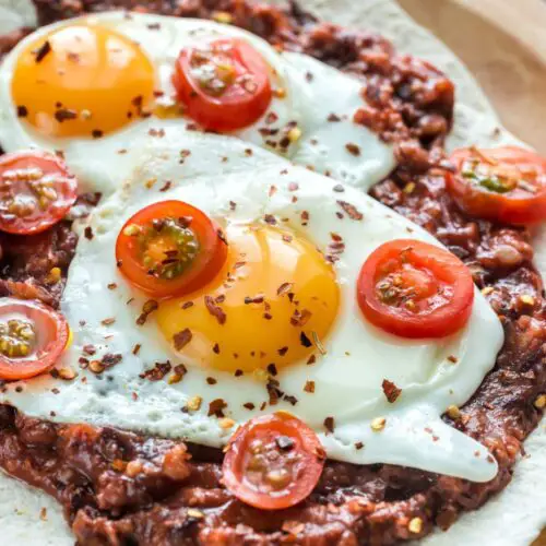 A white plate with baked huevos rancheros, featuring a baked egg in a rich tomato sauce topped with fresh cilantro