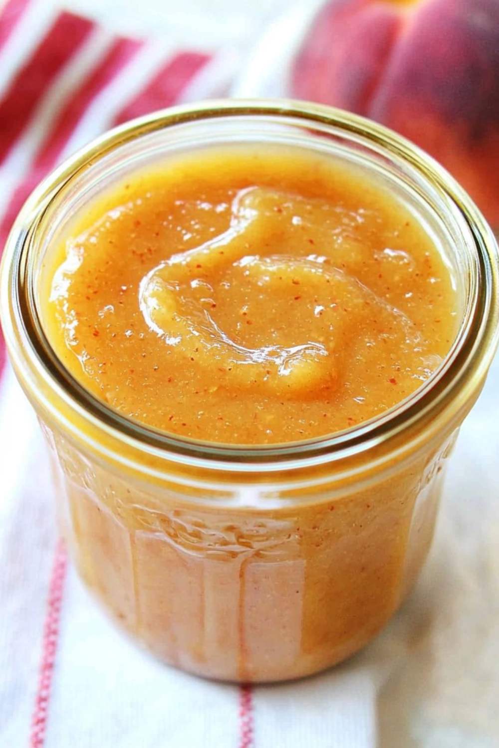 peach butter in glass jar and peach and napkin is partially visible in background