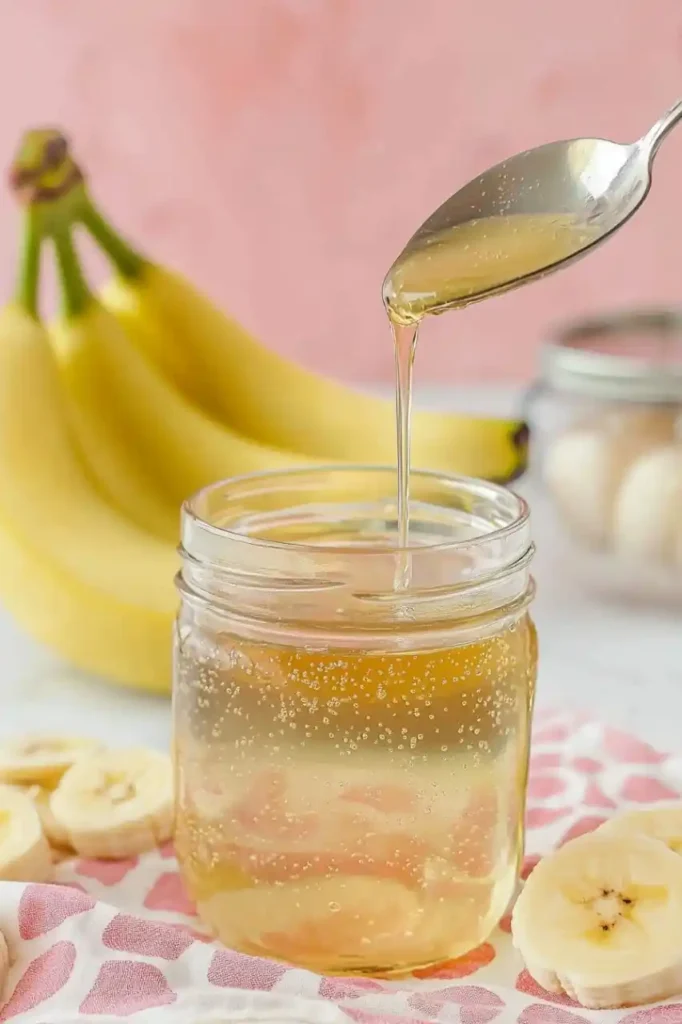 banana syrup in jar and three bananas in the background are partially visible