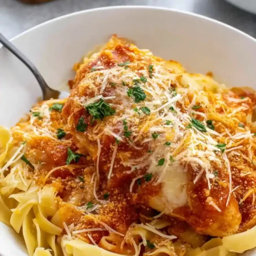 Crockpot Parmesan Chicken served over noodles garnish with cheeese