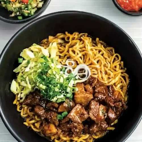 Gya kaku garlic noodle is place in black pan , and nearbly bowl filled with slices of tomatois placed