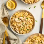 Three bowls of creamy chicken noodle pasta garnished with chopped parsley, arranged on a light surface.
