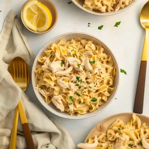 Three bowls of creamy chicken noodle pasta garnished with chopped parsley, arranged on a light surface.