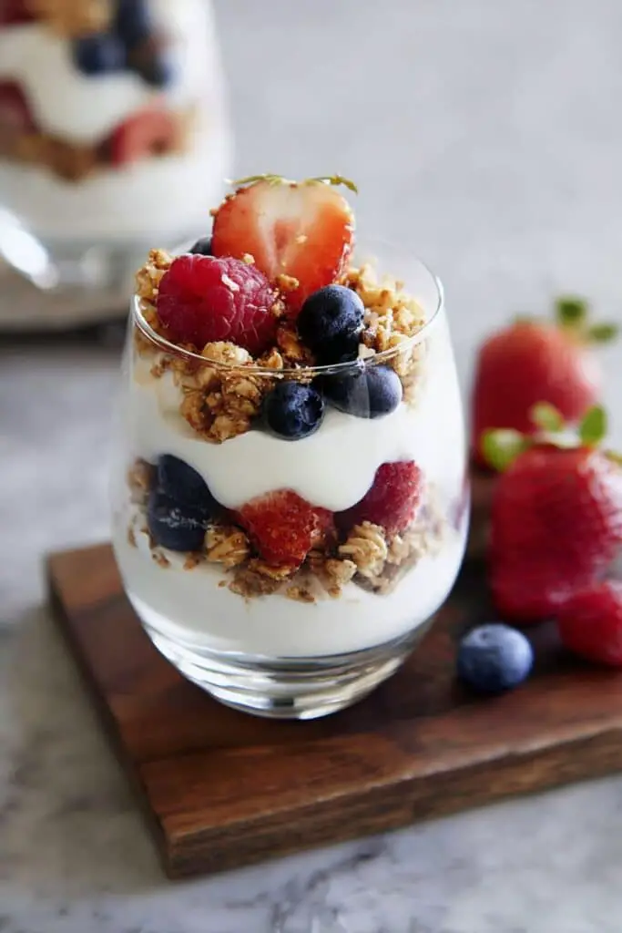 Glass of Greek Yogurt Parfait place on wooden table and berries scatter around